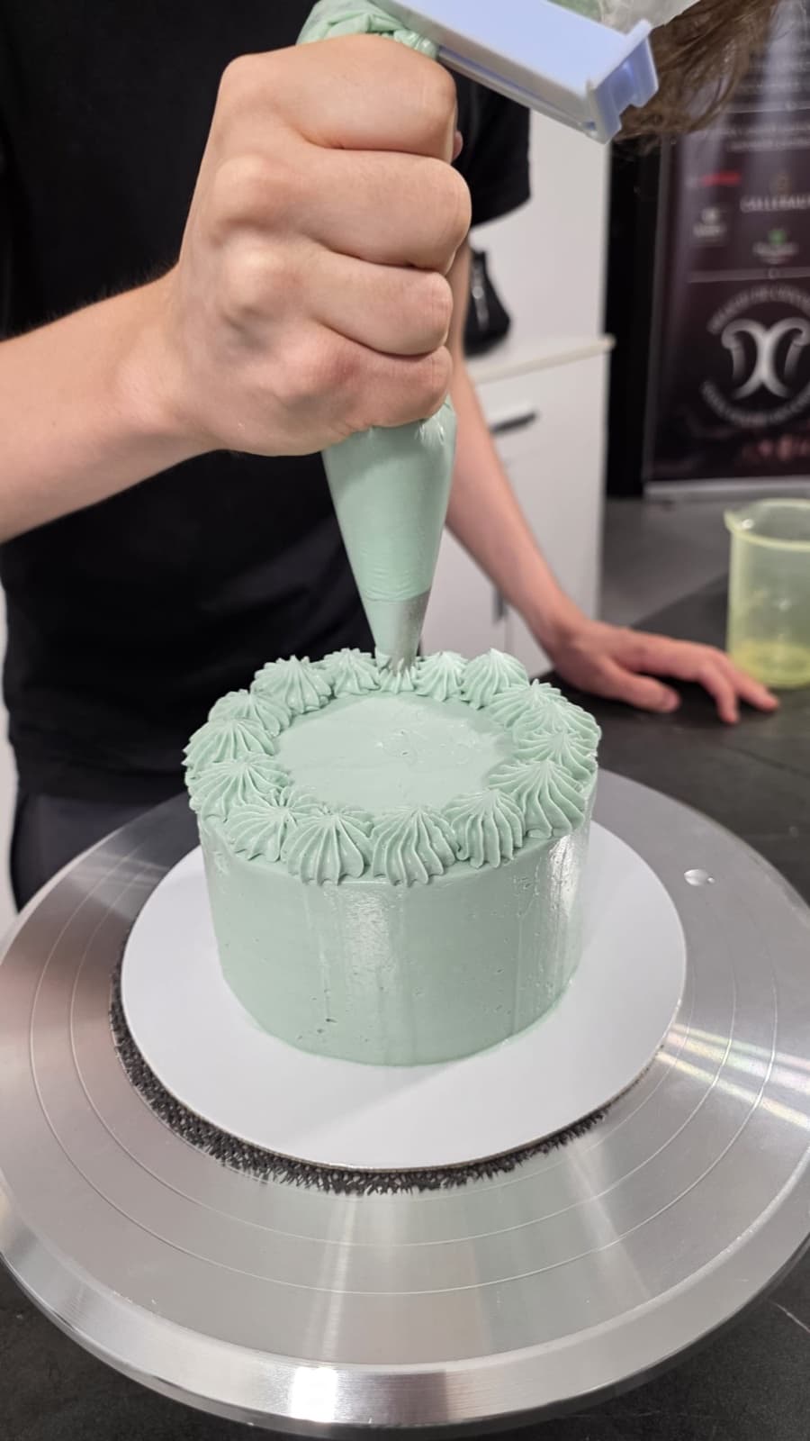 Cofetarul decorând un tort cu cremă verde mentă, în atelier